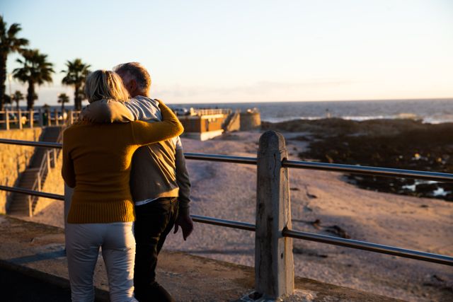 Rear view of a senior Caucasian couple in love enjoying time in nature together, standing on a promenade, embracing, during a sunset