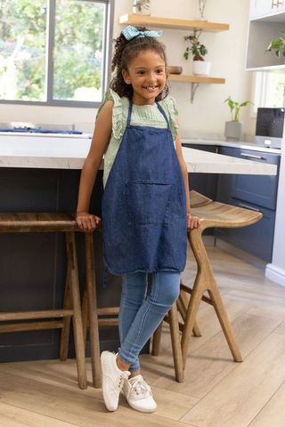 Young girl smiling leaning on marble kitchen island wearing denim apron