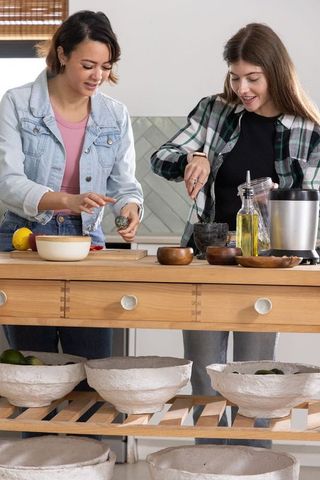 Diverse women preparing meal together at kitchen island chopping herbs and grinding spices