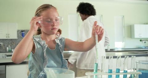 Young girl conducting science experiment with pipette and test tubes in classroom lab