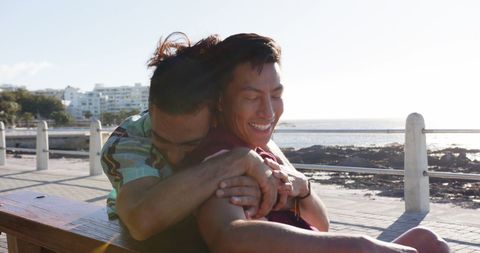 Happy Gay Couple Embracing Oceanfront Bench on Sunny Day