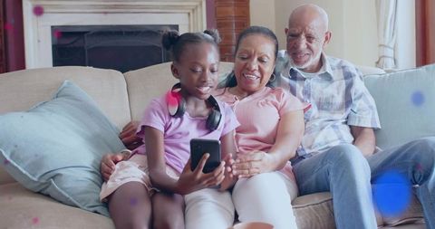Granddaughter showing smartphone to grandparents on sofa, smiling family bonding moment