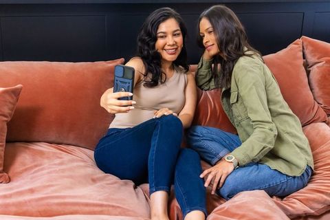 Diverse female friends taking selfie on cozy salmon velvet sofa relaxing together