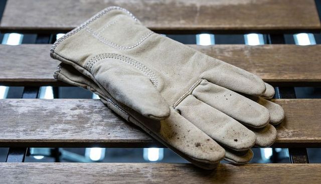 Tan leather work gloves resting on weathered wood bench with grease stains