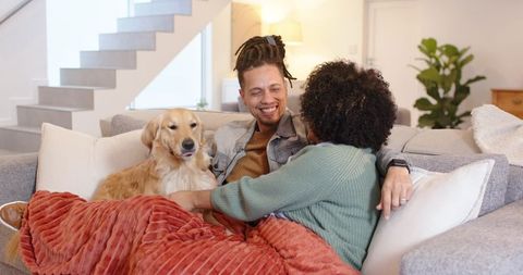 African American couple cuddling on couch with golden retriever under cozy blanket