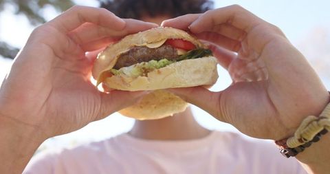 Person Enjoying Hamburger Outdoor on Sunny Day