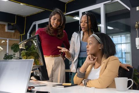 Diverse female professionals collaborating around monitor in modern office workspace