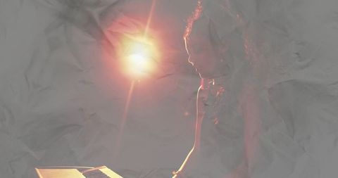 Woman playing keyboard under dramatic spotlight with lens flare and moody silhouette