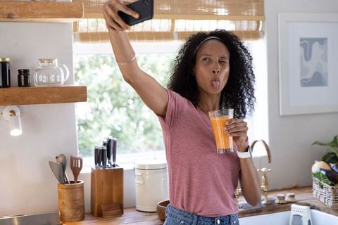 Taking playful selfie holding orange juice in bright modern kitchen
