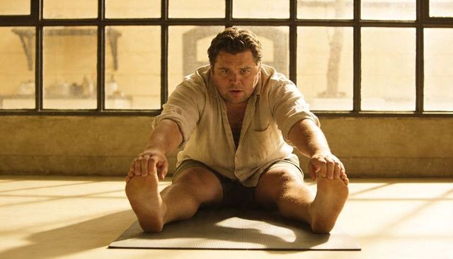 Man stretching forward fold on yoga mat in sunlit studio, mindfulness and fitness