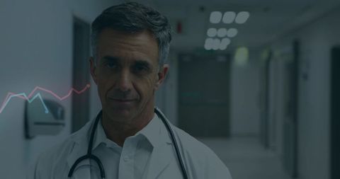 Mature male doctor standing in clinic corridor wearing lab coat and stethoscope