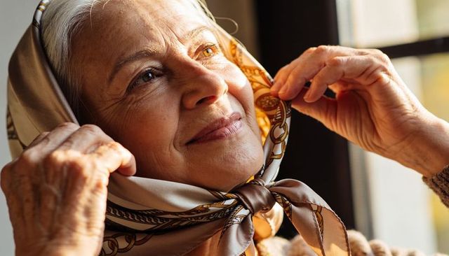 Smiling senior woman adjusting patterned silk headscarf by sunlit window
