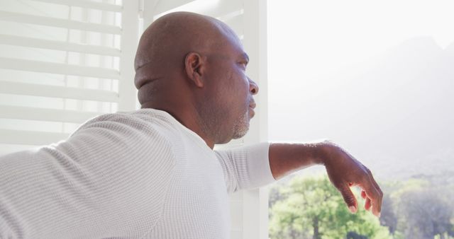 Image of a mature African American man standing by a window, looking out with a serene expression. This depiction is ideal for ads and articles focusing on mental health, relaxation, introspection, and mindfulness. Suitable for wellness blogs, lifestyle magazines, and meditative practice promotions.