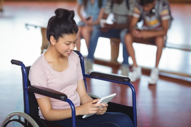 Schoolgirl in wheelchair using digital tablet while classmates are in the background. Useful for topics on education, technology, inclusion, diversity, and accessibility in schools. Ideal for promoting inclusive education, digital learning tools, and support for students with disabilities.
