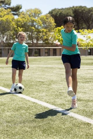 Schoolgirls playing soccer on sunlit field kicking ball during outdoor pe practice