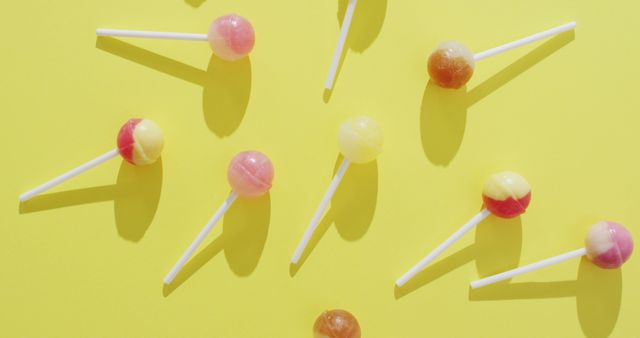 Assorted lollipops in various colors scattered on a vibrant yellow background. Great for promotional material relating to candy, sweets, and desserts. Use this image for advertisements, social media content, or decorative purposes for events or websites oriented around confections and fun themes.