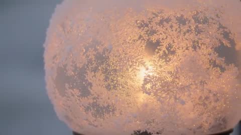 Pulling back from frosted globe lamp casting warm amber glow at winter dusk
