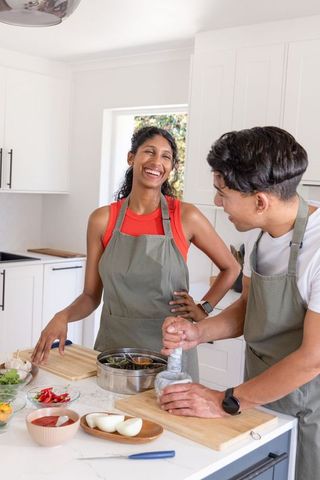 Partners preparing fresh meal in contemporary kitchen using mortar and pestle, laughing