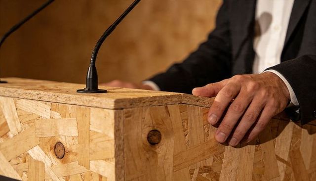 Business speaker presenting behind osb wood podium with gooseneck microphones, close-up hands
