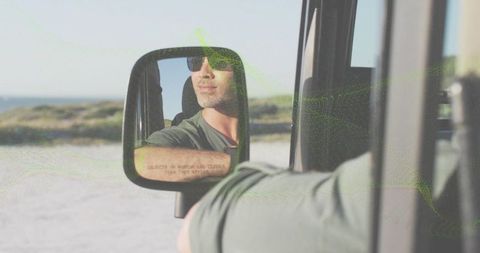 Man leaning out car window at beach wearing sunglasses reflecting in side mirror