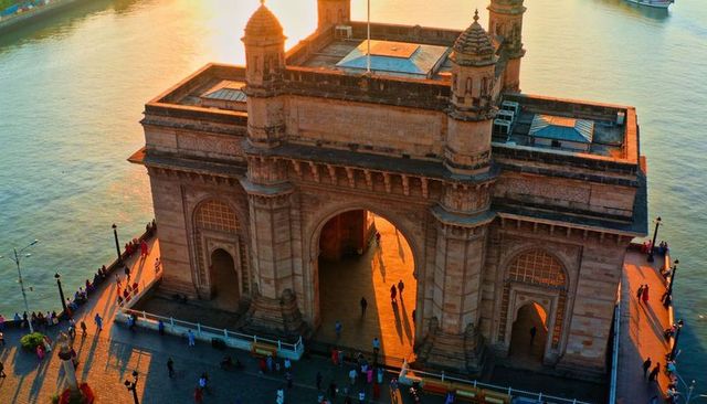 Gateway of india at sunset casting long shadows, crowds in colorful saris