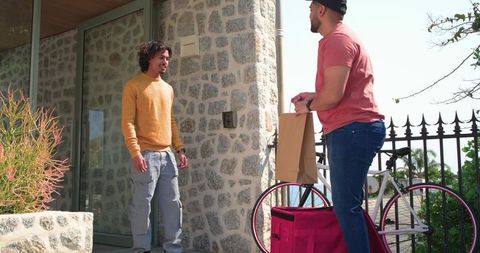Courier delivering takeout to resident at front doorstep with bicycle and reusable bag
