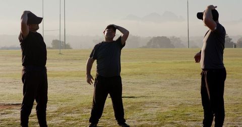 Three men stretching on misty dawn sports field wearing baseball caps and athletic clothing