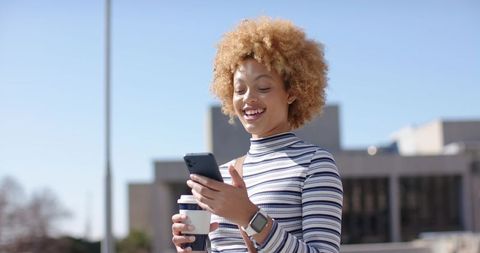 Woman checking smartphone with coffee cup in striped top and smartwatch urban plaza