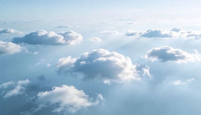 Sunlit fluffy cumulus clouds drifting across serene high-altitude sky with soft sunbeams