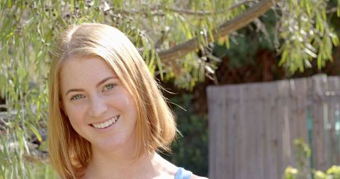 Smiling Blonde Woman Enjoying Tranquil Backyard Under Tree Branches