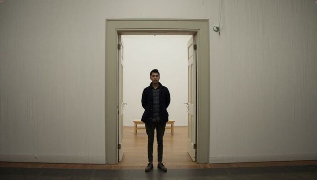 Solitary man standing in minimalist gallery doorway with wooden bench