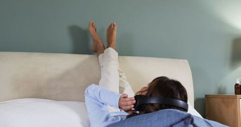 Woman Relaxing on Bed with Headphones and Feet on Wall
