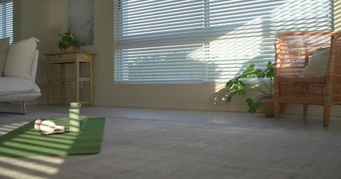 Sunlit yoga mat with water bottle and headphones near window blinds in minimal living room