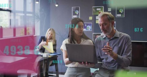Colleagues collaborating over laptop reviewing charts and financial data in modern office