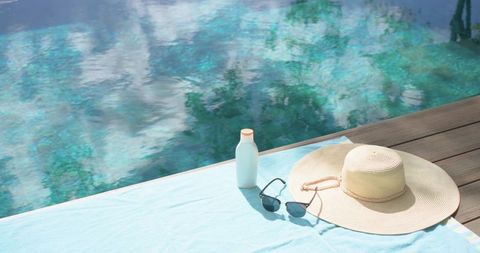 Sunlit poolside towel with straw hat sunglasses and sunscreen inviting relaxation