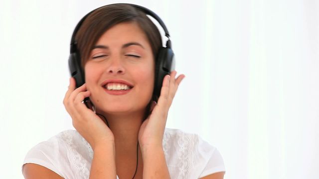 Young brunette woman enjoying music with headphones against a plain white background. Ideal for use in advertisements for music streaming services, audio equipment, relaxation and leisure activities, or technology and lifestyle content.