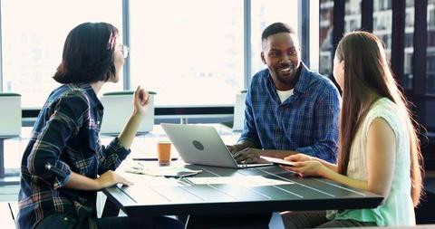 A diverse group of young professionals is engaged in a discussion at a bright office space, with copy space. Their collaboration could signify a team meeting or a creative brainstorming session.