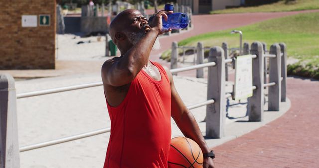 Senior african american man with basketball drinking water on the court near the beach - Download Free Stock Photos Pikwizard.com