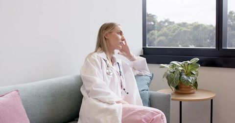 Female doctor sitting on sofa in staff lounge contemplating outside view