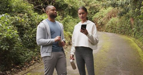 Diverse friends walking forest trail checking phone while holding reusable water bottles