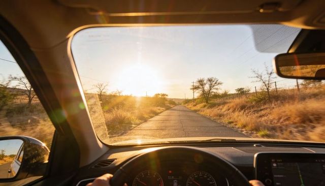 Driving through sunlit rural road at golden hour from inside car with navigation