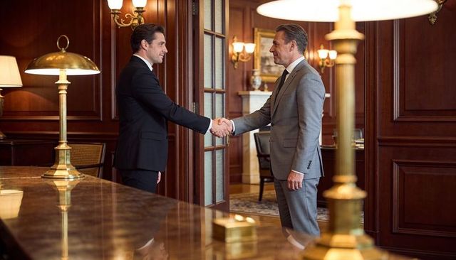 Shaking hands in wood-paneled office with glossy table and brass lamps, two businessmen