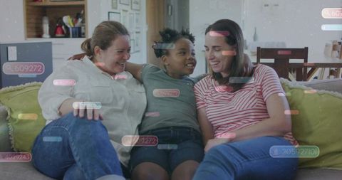 Smiling same-sex parents hugging child on cozy living room sofa with digital tags overlay