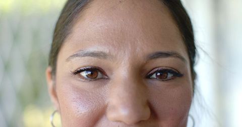 Gazing brown-eyed woman showing natural skin texture, subtle eyeliner, soft glow