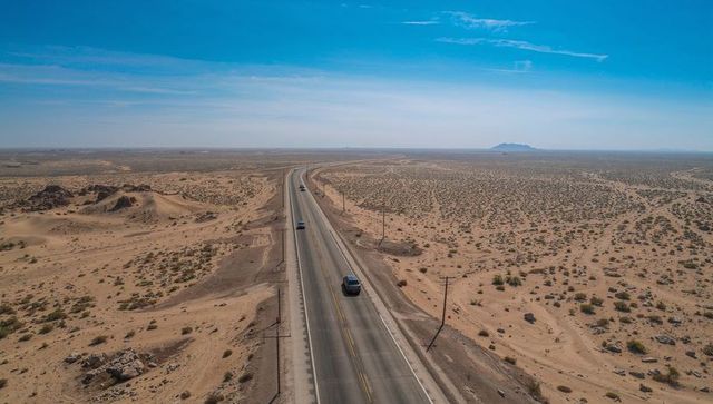 Cutting two-lane highway stretching across arid plain with distant horizon, solitary cars