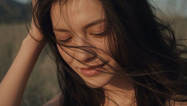 Serene asian woman closing eyes with windblown hair in sunlit meadow portrait