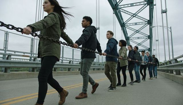 Diverse group walking linked by heavy chain on steel bridge showing unity and teamwork