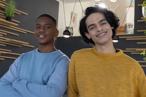 Two smiling young men standing in contemporary coworking lounge wearing casual sweaters