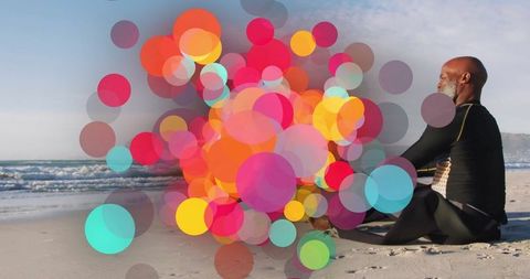 Senior Man in Wetsuit Meditating on Beach with Colorful Bokeh