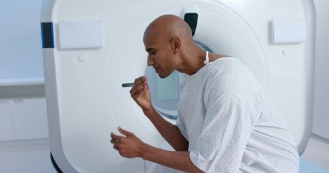 African man sitting on ct scanner table holding pill while preparing for diagnostic ct scan